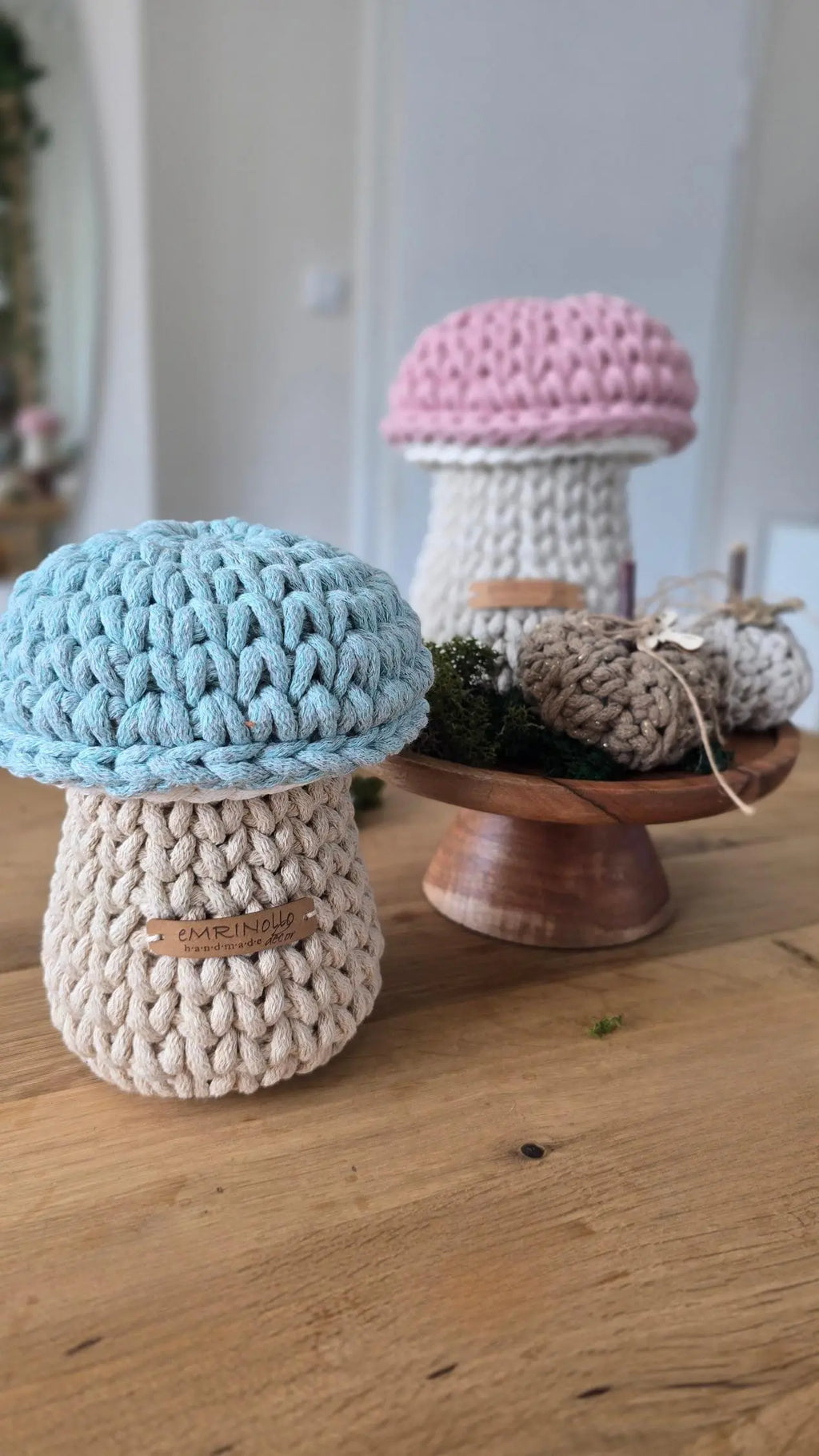 Handgehäkelter kleiner Aufbewahrungskorb in Pilzform aus dickem beigem Textilgarn mit einer salbeigrünen Pilzkappe als Deckel, freigestellt auf einer hellen Wickelkommode aus Holz im skandinavischen Kinderzimmer.