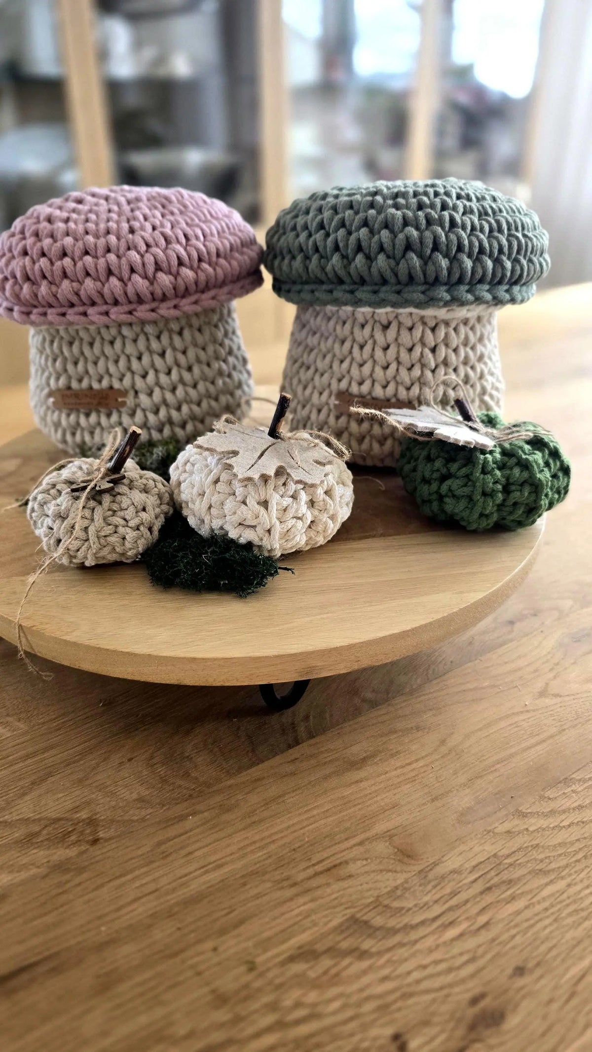 Gehäkeltes kleines Utensilo in Pilzform aus beiger Baumwollschnur mit einer salbeigrünen Kappe als abnehmbarer Deckel, herbstlich dekoriert mit kleinen Holzfiguren in einem hellen Kinderzimmerregal.
