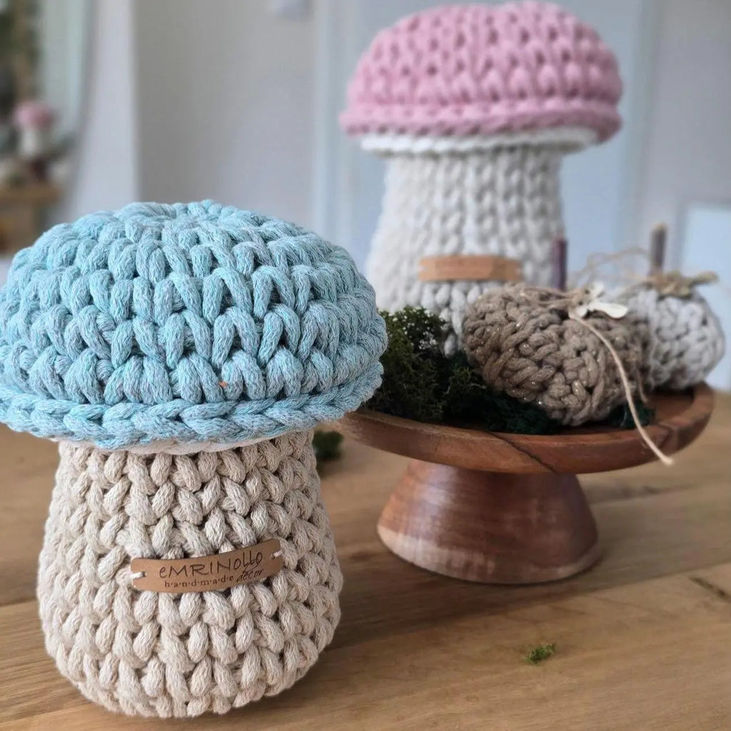Handgehäkelter kleiner Aufbewahrungskorb in Pilzform aus dickem beigem Textilgarn mit einer salbeigrünen Pilzkappe als Deckel, freigestellt auf einer hellen Wickelkommode aus Holz im skandinavischen Kinderzimmer.